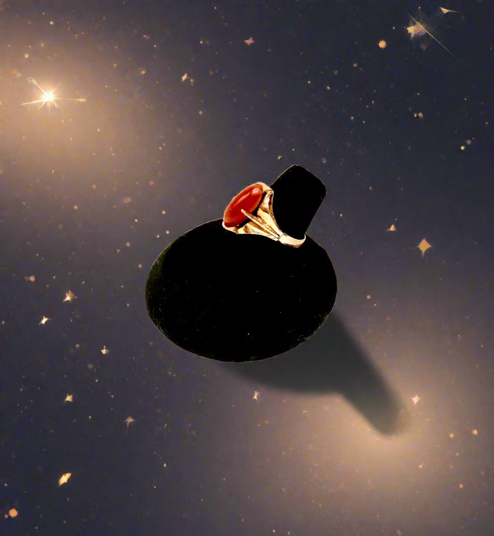 Gold ring with a red stone on a black stand against a light gray background