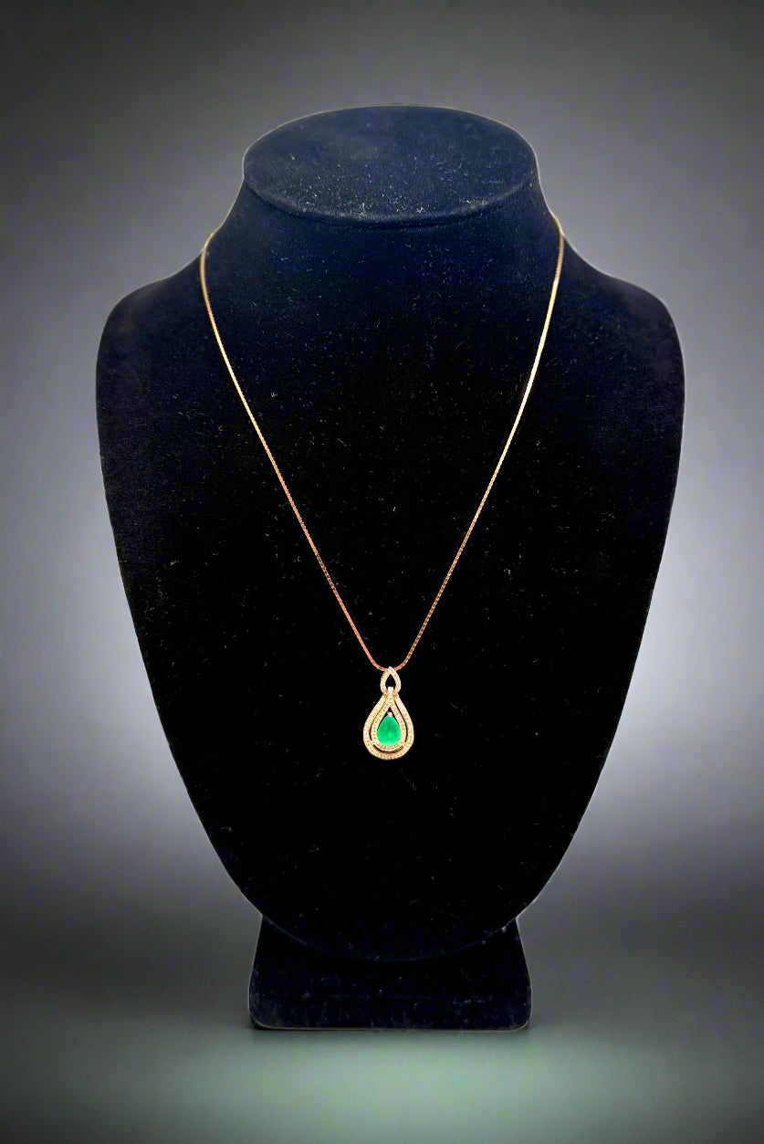 Gold necklace with a green pendant on a black mannequin bust against a white background