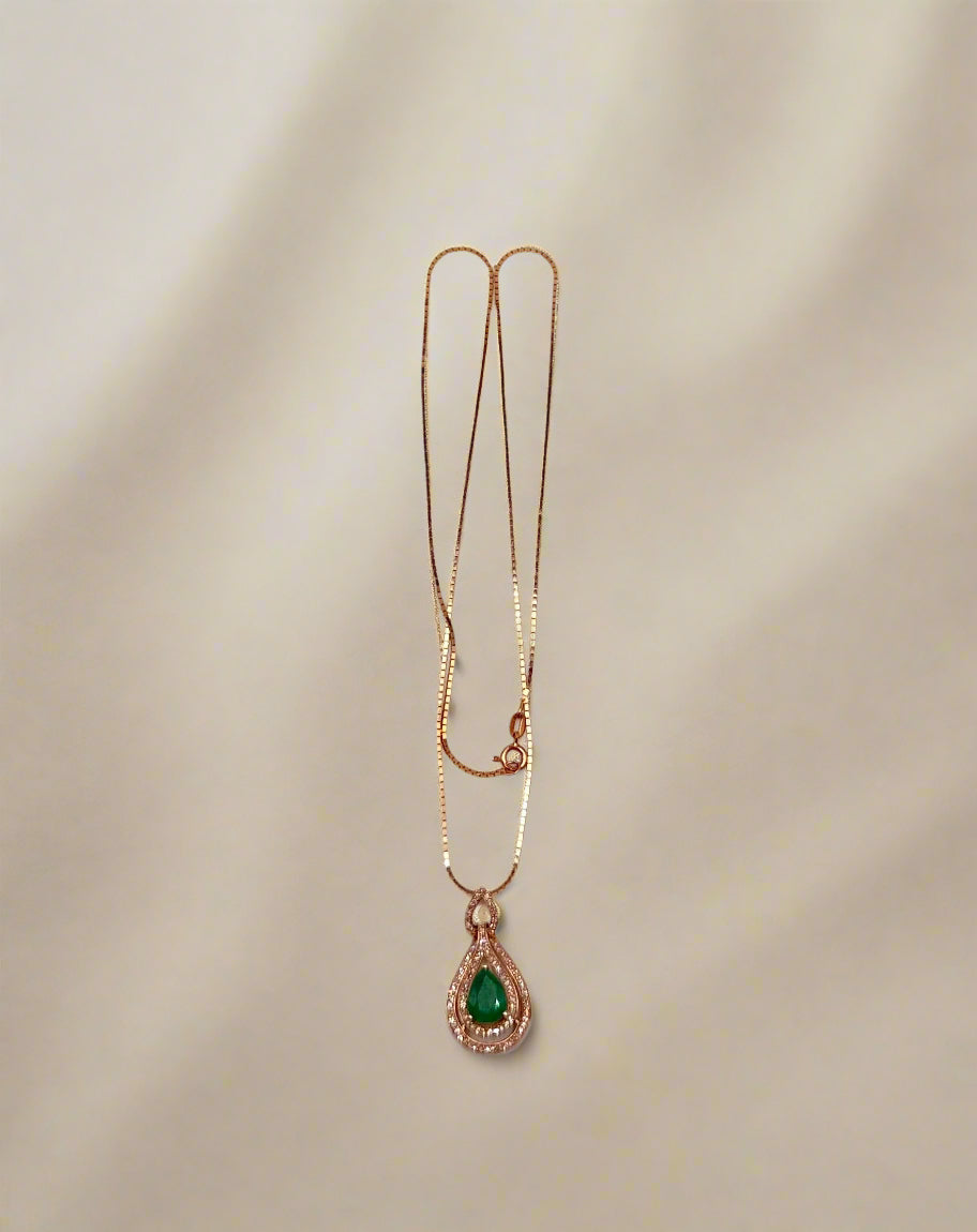 Gold necklace with a green teardrop pendant on a light gray background