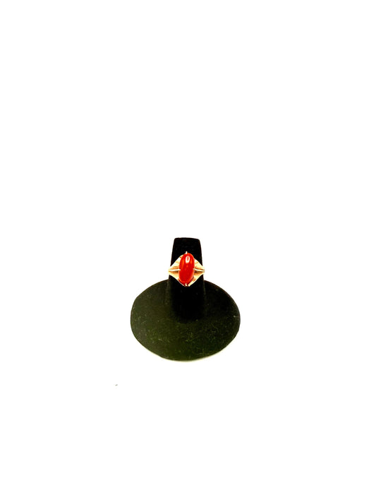 Ring with a red gemstone on a black stand against a white background